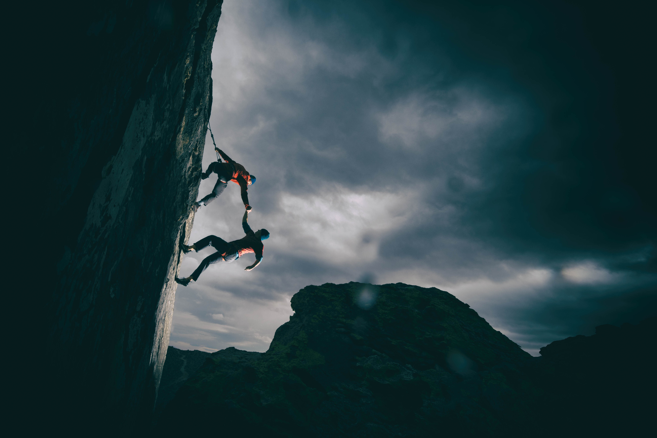 Two climbers on a cliff. Friend catches partner as he falls off the mountain. Helping each other.